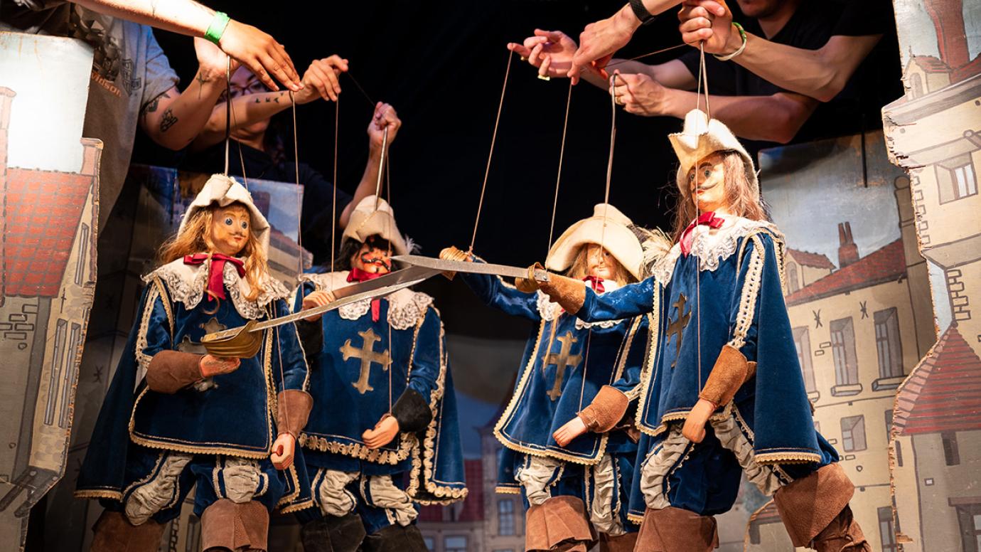 چندین عروسک گردان در حال اجرای نمایش صحنه نبرد عروسکی