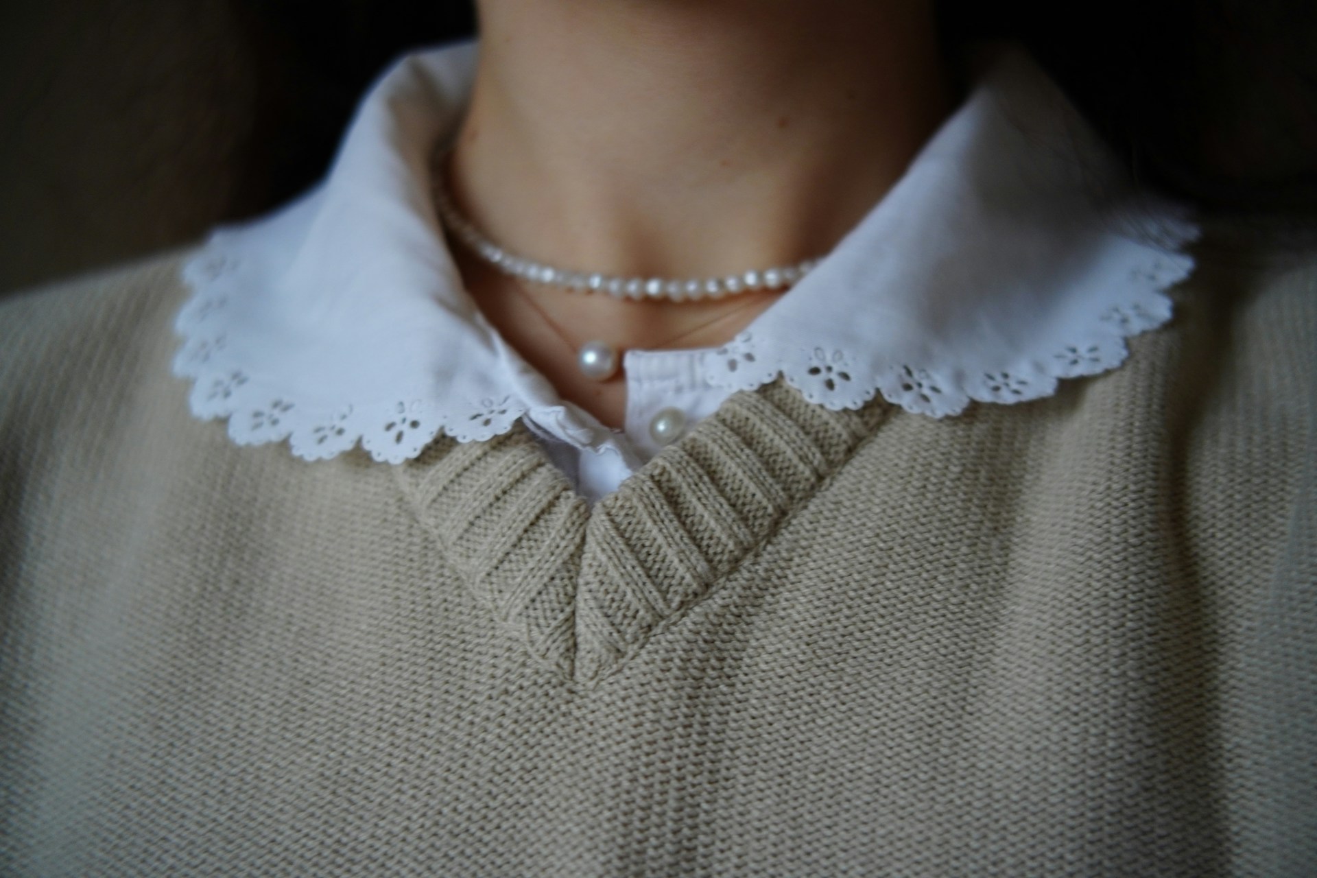 خانومی با پلیور یقه هفت نروژی کرمی همراه گردنبند مروارید و تیشرت نخی سفید